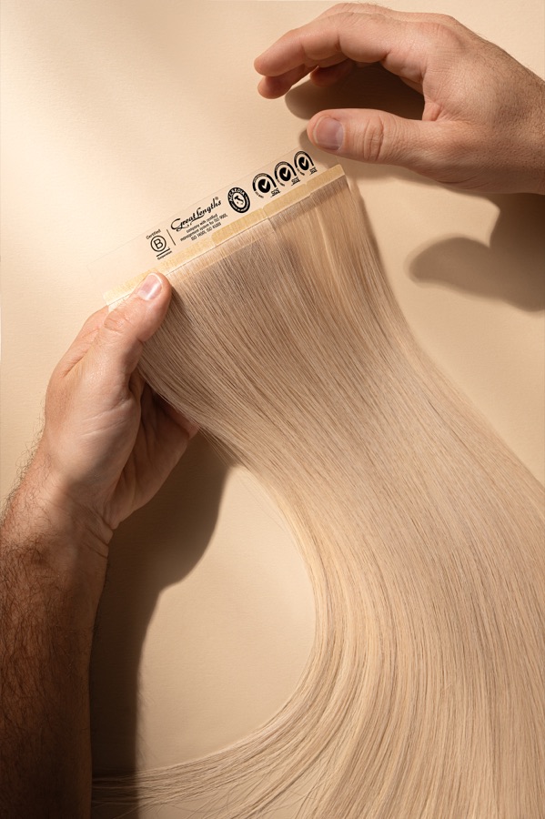 A stylist holding a blonde Great Lengths tape-in extension weft
