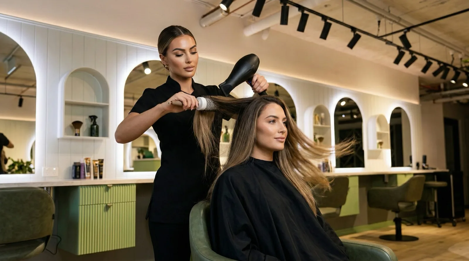 Hair Avenue stylist blow-drying a smiling client in the chair with the product wall behind